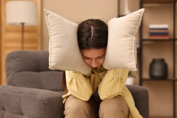 Obraz premium Annoyed woman covering her ears with pillows due to loud sound at home