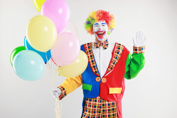 Happy clown with colorful balloons waving on light background