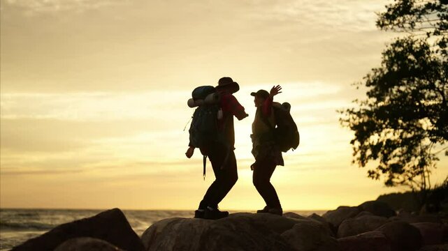 Dancing backpackers on coast of sea, slow motion, silhouette, local tourism. Positive emotions and good mood, hikers enjoying beautiful seascape in sunset, weekend trip in summer vacation, full-length