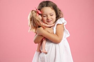 Cute little girl embracing her doll on pink background