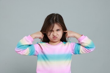 Annoyed little girl covering her ears from loud sound on grey background