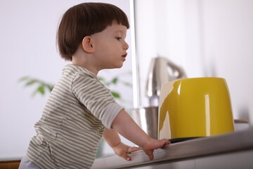 Little boy playing with toaster in kitchen. Dangerous situation