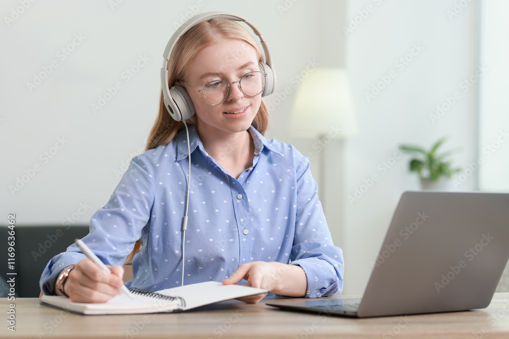 Poster interpreter in headphones taking notes while working with laptop at table indoors