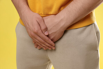 STD (sexually transmitted diseases). Man suffering from symptoms on yellow background, closeup