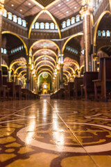 Vertical photo of wide central hallway with classical architecture with wooden benches of the Basilica of Our Lady of the Angels in Cartago, Costa Rica