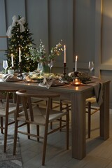 Christmas table setting with stylish dishware, glasses and burning candles in festive decorated room