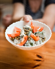 Hand Holding Bowl of Tomato, Pea, and Cucumber Salad on Wooden Table