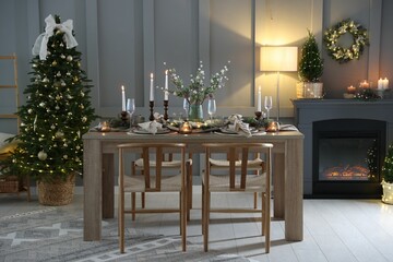 Christmas table setting with stylish dishware, glasses and burning candles in festive decorated room