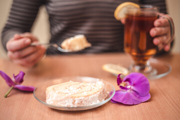 Person Enjoying Tea with Lemon and Dessert at a Wooden Table