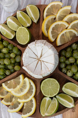 wooden plate with snacks - lemon, lime, cheese, gooseberry, berry