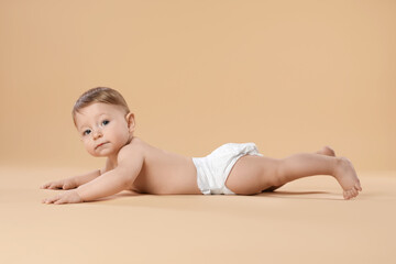Obraz premium Cute little baby in diaper crawling on beige background