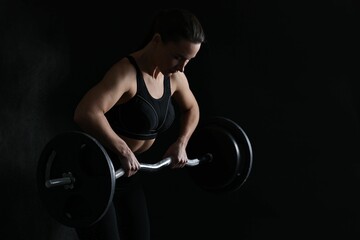 Woman training with barbell against black background