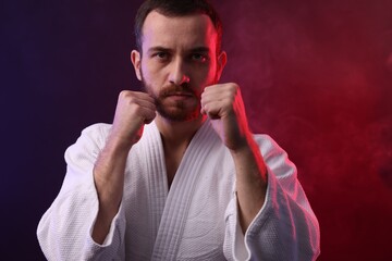 Karate fighter wearing uniform in color lights and smoke