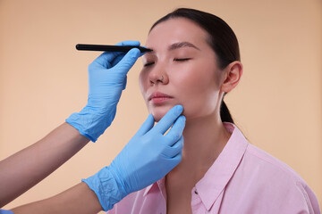 Doctor drawing marks on patient's nose for plastic surgery operation against beige background,...