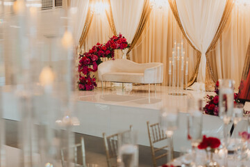 Luxurious Wedding Stage with Gold Drapes, Floral Arrangements, and Elegant White Seating for a Romantic Reception
