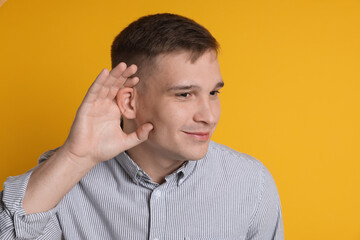 Man showing hand to ear gesture on orange background