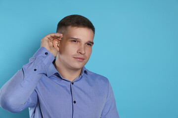 Man showing hand to ear gesture on light blue background, space for text
