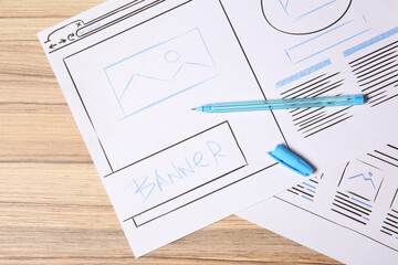 Website development. Sketches of wireframes and pen on wooden table, flat lay