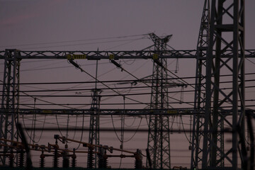 Electric substation equipped with security fencing and power lines, outdoor environment at dusk...