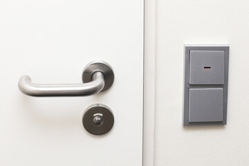 Hotel room door with a silver handle and light switch nearby. Modern and functional setup. Secure entrance interior design. White bright door room interior view.