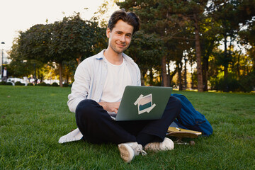 A man sits on the grass in a park using a laptop, enjoying the outdoors.