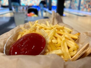 A basket of crispy golden fries with a cup of ketchup in the foreground, set against a vibrant...