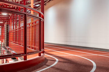 Close-up photo of a curved red railing along an elevated indoor running track around a gymnasium.