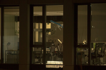 Office Building with Large Windows Viewed from Outside at Night. An office space with large, illuminated windows is captured from an exterior perspective during the evening or night.