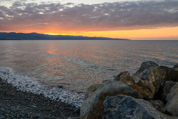 Golden sunset over tranquil sea and rocky shoreline illuminating a serene evening
