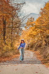 Fototapeta premium Young woman enjoying a peaceful walk on a scenic road amidst vibrant autumn foliage