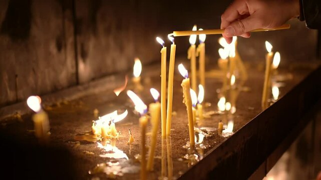 A group of thin burning candles in a church. A parishioner lights a candle after a church service in Orthodox or Catholic church. Christian Christmas or Easter
