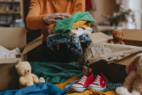 Woman sorting an old out-of-use kid toy, clothes and shoes in box for charity or upcycling