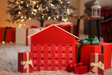 Red advent calendar with gift boxes on floor near Christmas tree at home