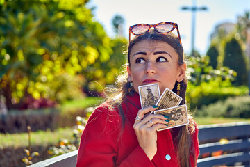 Tarot cards with symbolic illustrations held by a woman in red coat with green nails, gold...