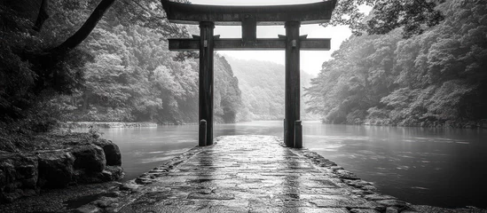 Fotobehang A tranquil and atmospheric image of a traditional Japanese torii gate standing tall in the middle of a serene lake surrounded by a misty forest  The monochrome © Waraporn
