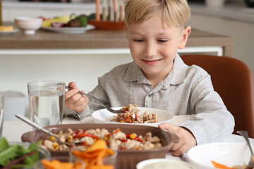 Cute little boy eating Fajita at table in kitchen