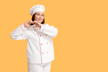 Young female chef making heart gesture on yellow background