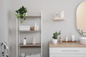 Stacks of clean towels with houseplants and cosmetic products on shelving unit in bathroom
