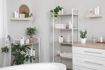 Stacks of clean towels with houseplants and cosmetic products on shelving unit in bathroom