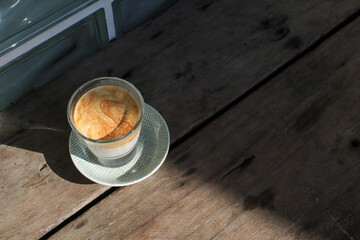 Dirty coffee latte in glass under sunlight and shadow on wooden board. Espresso layer on the top and chilled cold milk or cream at the bottom.