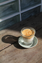 Dirty coffee latte in glass under sunlight and shadow on wooden board. Espresso layer on the top and chilled cold milk or cream at the bottom.