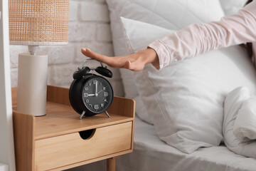 Young woman turning off alarm clock on table in bedroom, closeup
