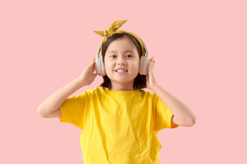 Cute little Asian girl in headphones on pink background
