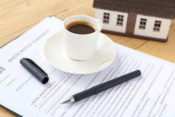 Blank house rental agreement with cup of coffee on wooden background, closeup