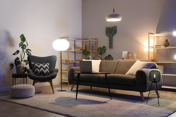 Interior of dark living room with black sofa, armchair and glowing lamps at night