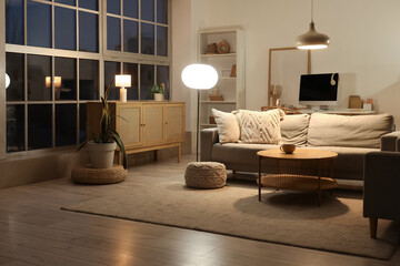 Interior of living room with grey sofa, drawers and glowing lamps