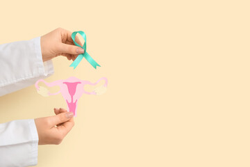 Female doctor hands with turquoise ribbon and paper uterus on beige background. Cervical Health...