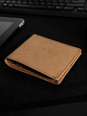 Blank brown men's leather wallet between gadgets on black background, perfect for leather industry catalog design