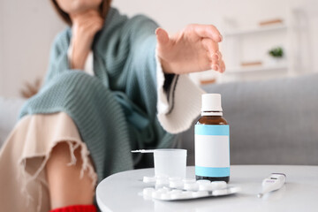 Sick young woman taking cough syrup from table at home, closeup