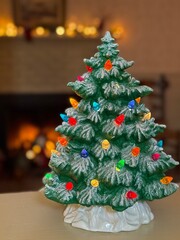 Festive vintage style ceramic Christmas tree with vibrant multicolored lights, displayed near a warm and cozy fireplace, creating a nostalgic holiday ambiance and happy seasonal charm.